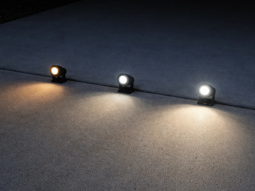 Three outdoor patio lights projecting different brightness levels onto a concrete surface.